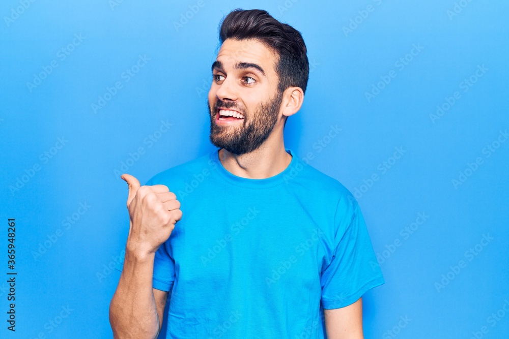 Young handsome man with beard wearing casual t-shirt pointing thumb up to the side smiling happy with open mouth Young handsome man with beard wearing casual t-shirt pointing thumb up to the side smiling happy with open mouth