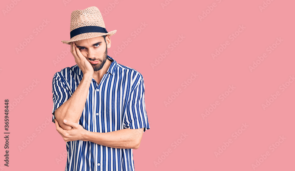 Young handsome man with beard wearing summer hat and striped shirt thinking looking tired and bored with depression problems with crossed arms. Young handsome man with beard wearing summer hat and striped shirt thinking looking tired and bored with depression problems with crossed arms.