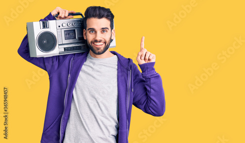 Young handsome man with beard listening to music using vintage boombox surprised with an idea or question pointing finger with happy face, number one