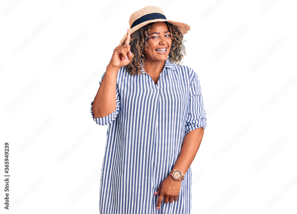 Young african american plus size woman wearing summer hat showing and pointing up with finger number one while smiling confident and happy.