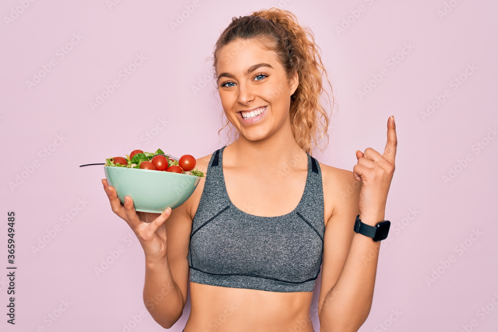 Φωτογραφία Young beautiful blonde sporty woman with blue eyes holding bowl with healthy sal