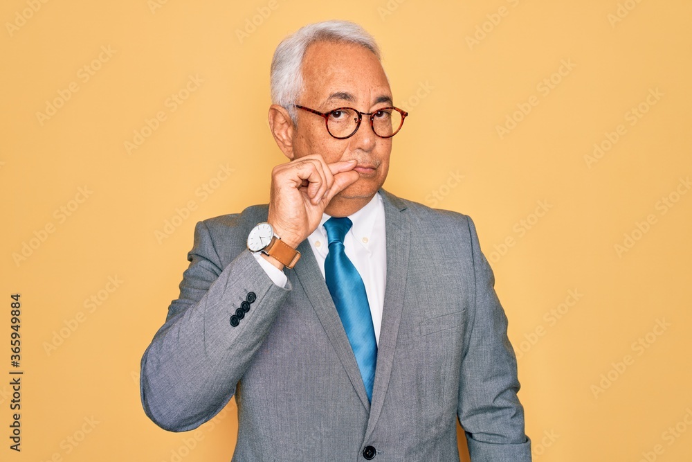Middle age senior grey-haired handsome business man wearing glasses over yellow background mouth and lips shut as zip with fingers. Secret and silent, taboo talking Middle age senior grey-haired handsome business man wearing glasses over yellow background mouth and lips shut as zip with fingers. Secret and silent, taboo talking