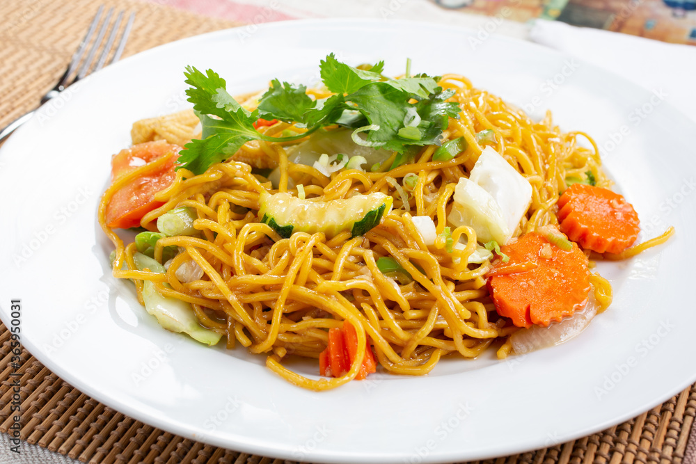 A view of a plate of chow mein, in a restaurant or kitchen setting.