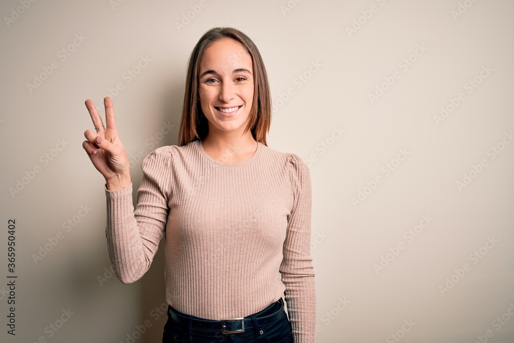 Young beautiful woman wearing casual sweater standing over isolated white background showing and pointing up with fingers number two while smiling confident and happy. Young beautiful woman wearing casual sweater standing over isolated white background showing and pointing up with fingers number two while smiling confident and happy.
