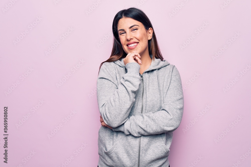Young beautiful sporty woman wearing sportswear standing over isolated pink background smiling looking confident at the camera with crossed arms and hand on chin. Thinking positive. Young beautiful sporty woman wearing sportswear standing over isolated pink background smiling looking confident at the camera with crossed arms and hand on chin. Thinking positive.