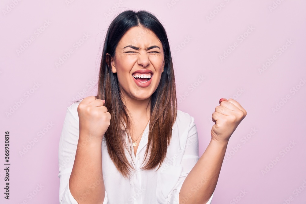 Young beautiful brunette woman wearing elegant shirt standing over isolated pink background celebrating surprised and amazed for success with arms raised and eyes closed Young beautiful brunette woman wearing elegant shirt standing over isolated pink background celebrating surprised and amazed for success with arms raised and eyes closed