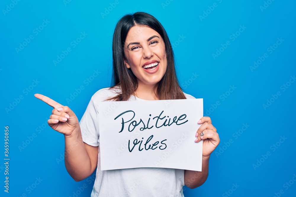 Young beautiful woman asking for optimist attitude holding paper with positive vibes message smiling happy pointing with hand and finger to the side Young beautiful woman asking for optimist attitude holding paper with positive vibes message smiling happy pointing with hand and finger to the side