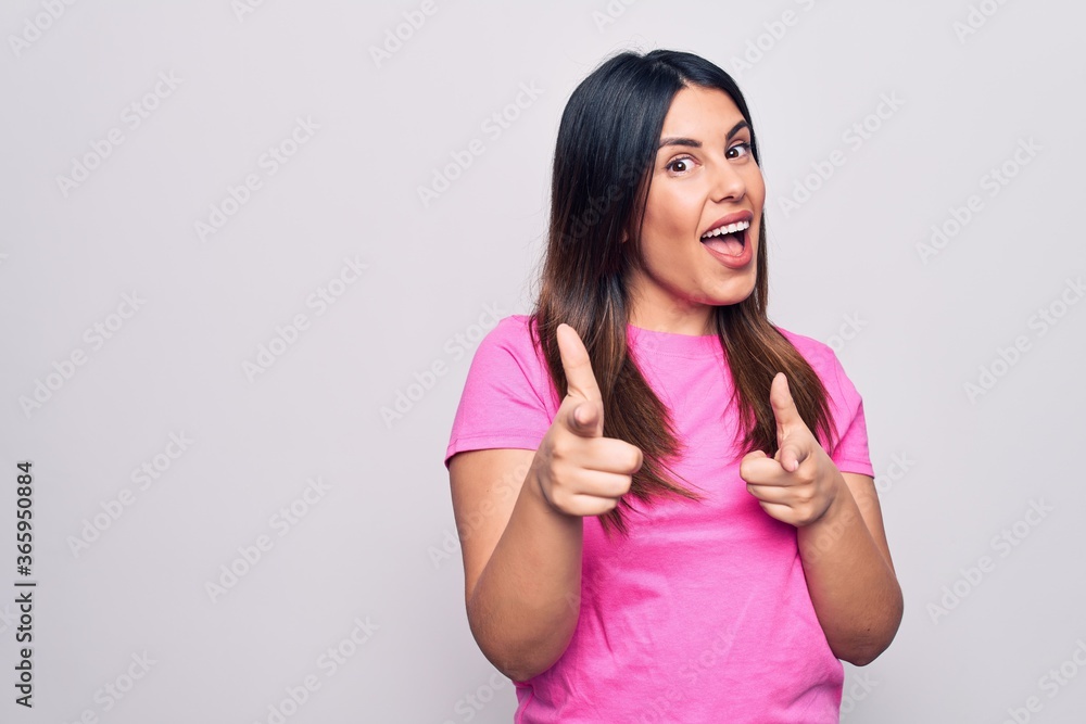 Young beautiful brunette woman wearing casual pink t-shirt standing over white background pointing fingers to camera with happy and funny face. Good energy and vibes. Young beautiful brunette woman wearing casual pink t-shirt standing over white background pointing fingers to camera with happy and funny face. Good energy and vibes.