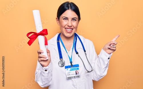 Young beautiful doctor woman wearing stethoscope holding diploma degree graduated smiling happy pointing with hand and finger to the side