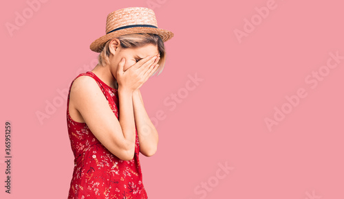 Young beautiful blonde woman wearing summer hat with sad expression covering face with hands while crying. depression concept.