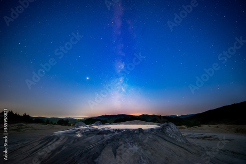 Milky way starry sky fading away into morning light with a muddy volcano in the foreground