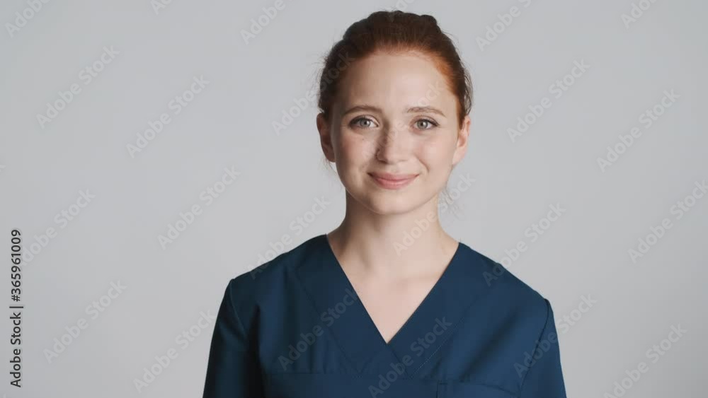 Young beautiful smiling doctor confidently looking in camera over gray background