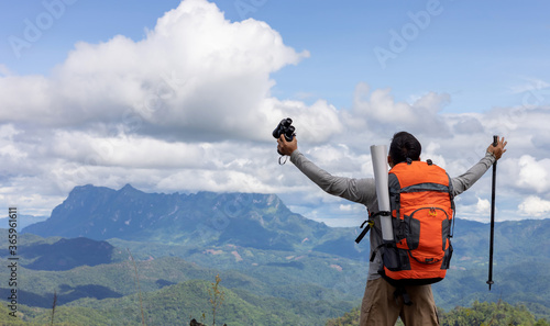 Young man with raised hands  and holding a binoculars standing on top of mountain