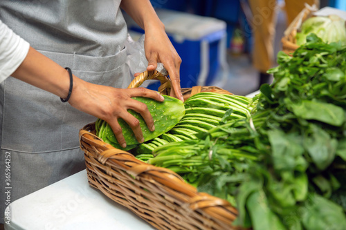 Latin woman putting nopales on a basket with other green vegetables for sell