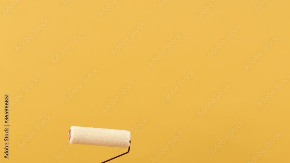 Woman hand holding paint roller moving up and down on empty space in yellow studio background Woman hand holding paint roller moving up and down on empty space in yellow studio background