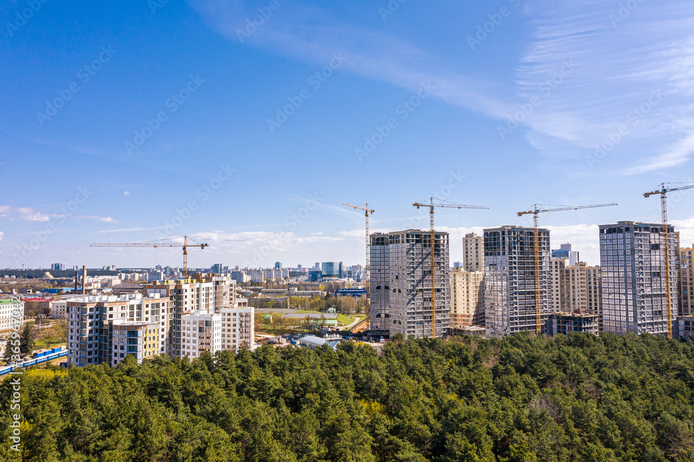high-rise apartment buildings construction site with working cranes against blue sky. aerial view from flying drone