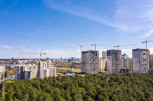 high-rise apartment buildings construction site with working cranes against blue sky. aerial view from flying drone
