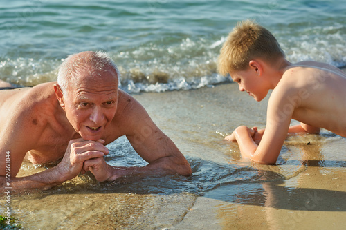 An elderly happy man with his grandson resting on the beach