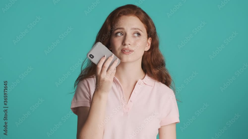Beautiful smiling redhead girl recording voice message to friend on smartphone over colorful background Beautiful smiling redhead girl recording voice message to friend on smartphone over colorful background