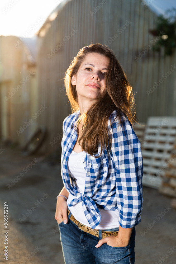 Smiling girl farmer standing on background of hothouse, posing on camera