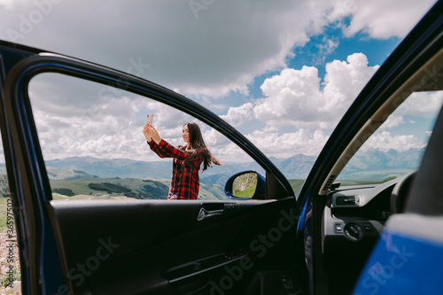 pretty woman travel by car and using smartphone on road trip vacations in mountains. Beautiful woman tourist travel by car to mountains and making a video call . Montenegro, Durmitor. 