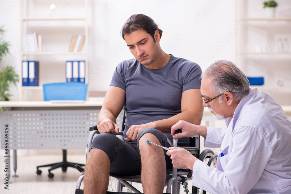 Young male patient in wheel-chair visiting old doctor Young male patient in wheel-chair visiting old doctor