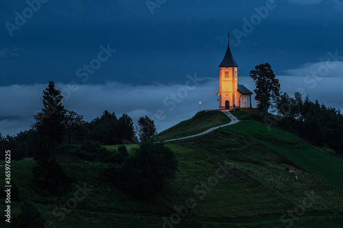 Jamnik, Slovenia - Blue hour at Jamnik with illuminated St. Primoz church on a foggy dawn. Julian Alps at background
