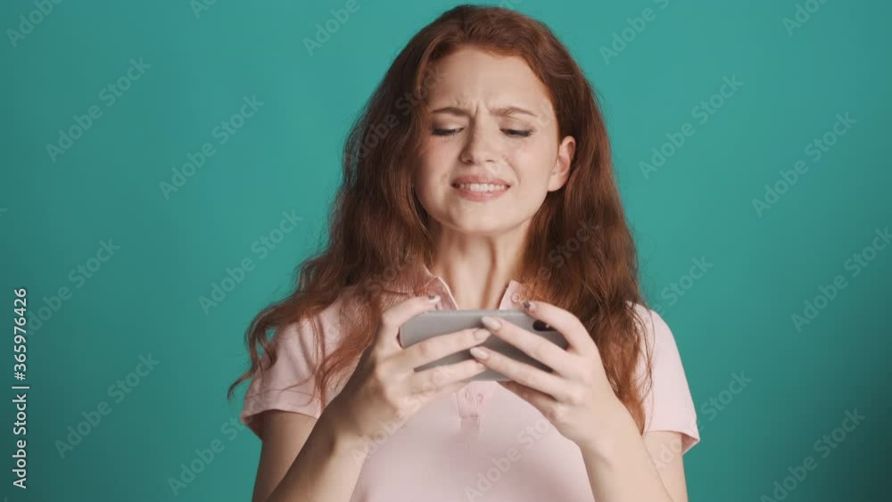 Attractive upset redhead girl playing in game on smartphone and losing over colorful background. Game away Attractive upset redhead girl playing in game on smartphone and losing over colorful background. Game away