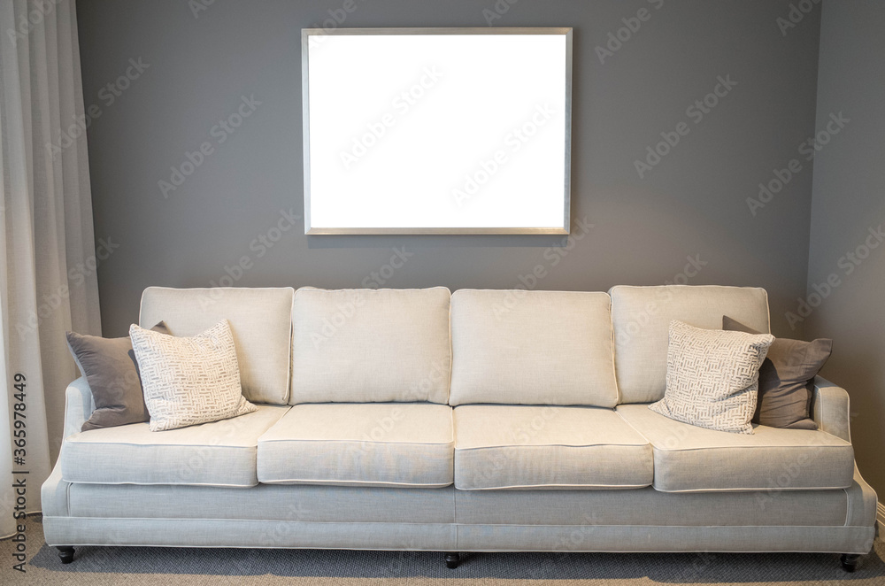 Blank white empty mock up template of a picture/art work with metal frame on living room/lounge wall with a neutral color sofa at front. Horizontal poster with copy space. Modern home/house interiors. Blank white empty mock up template of a picture/art work with metal frame on living room/lounge wall with a neutral color sofa at front. Horizontal poster with copy space. Modern home/house interiors.