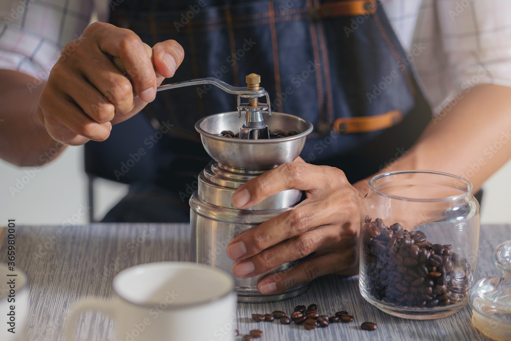 Barista with coffee grinder, grinding roasted coffee beans for a cup of coffee