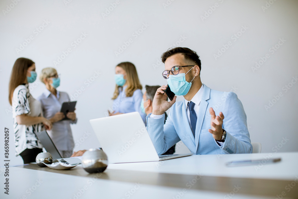 Young business man with medical protective mask works on a laptop and using mobile phone Young business man with medical protective mask works on a laptop and using mobile phone