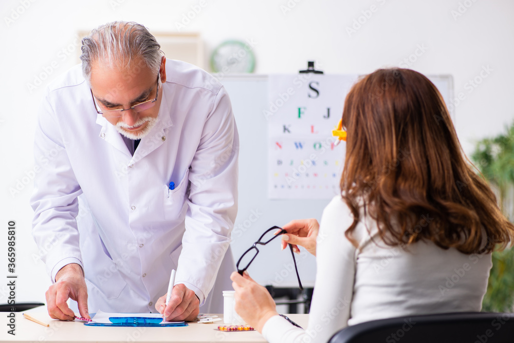 Fototapeta premium Young woman visiting old male doctor ophthalmologist