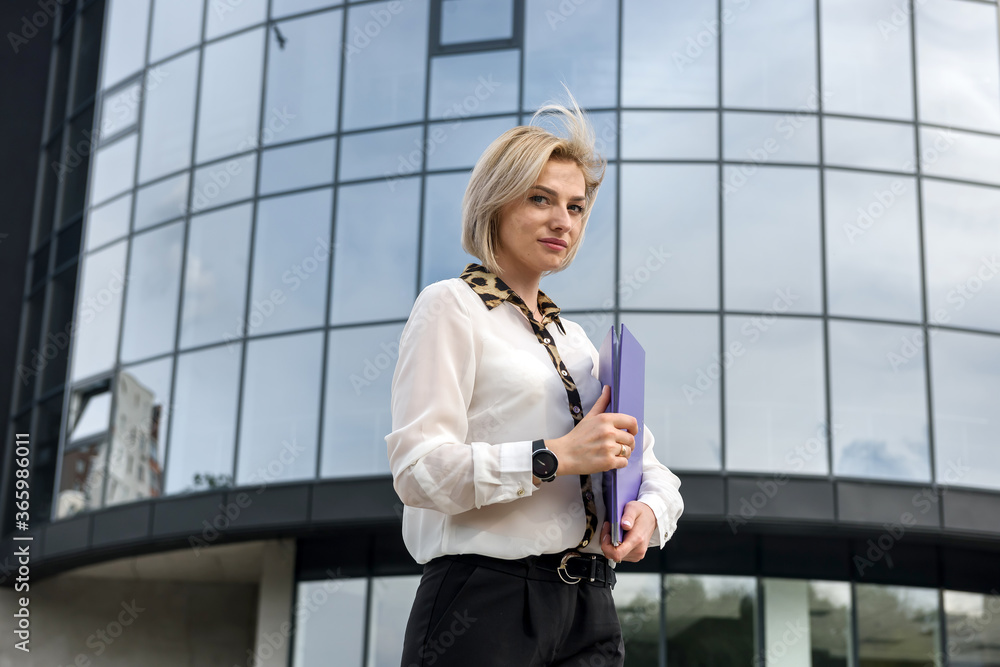 Business woman with folded standing before office building and looking in camera