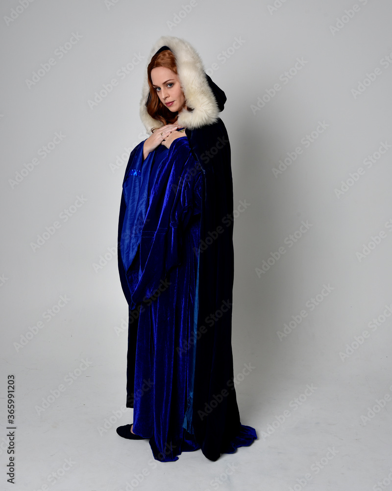 Naklejka premium Full length portrait of girl wearing long blue velvet gown with golden crown. sitting pose, isolated against a studio background.