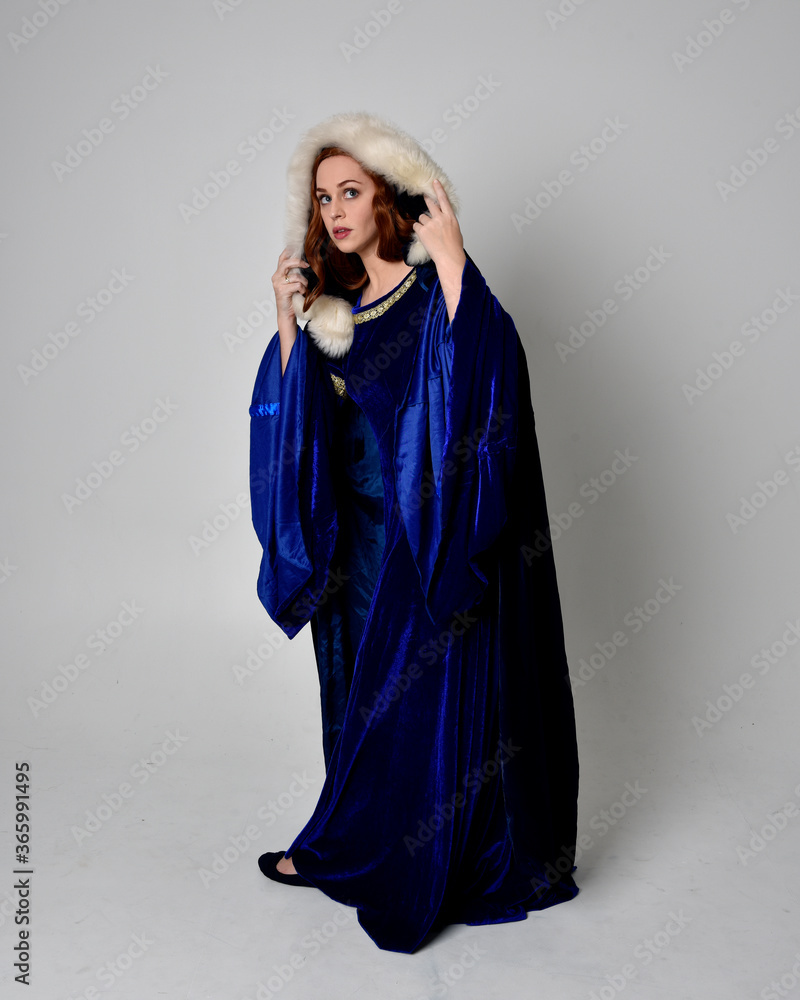 Full length portrait of girl wearing long blue velvet gown with golden crown. sitting pose, isolated against a studio background. Full length portrait of girl wearing long blue velvet gown with golden crown. sitting pose, isolated against a studio background.