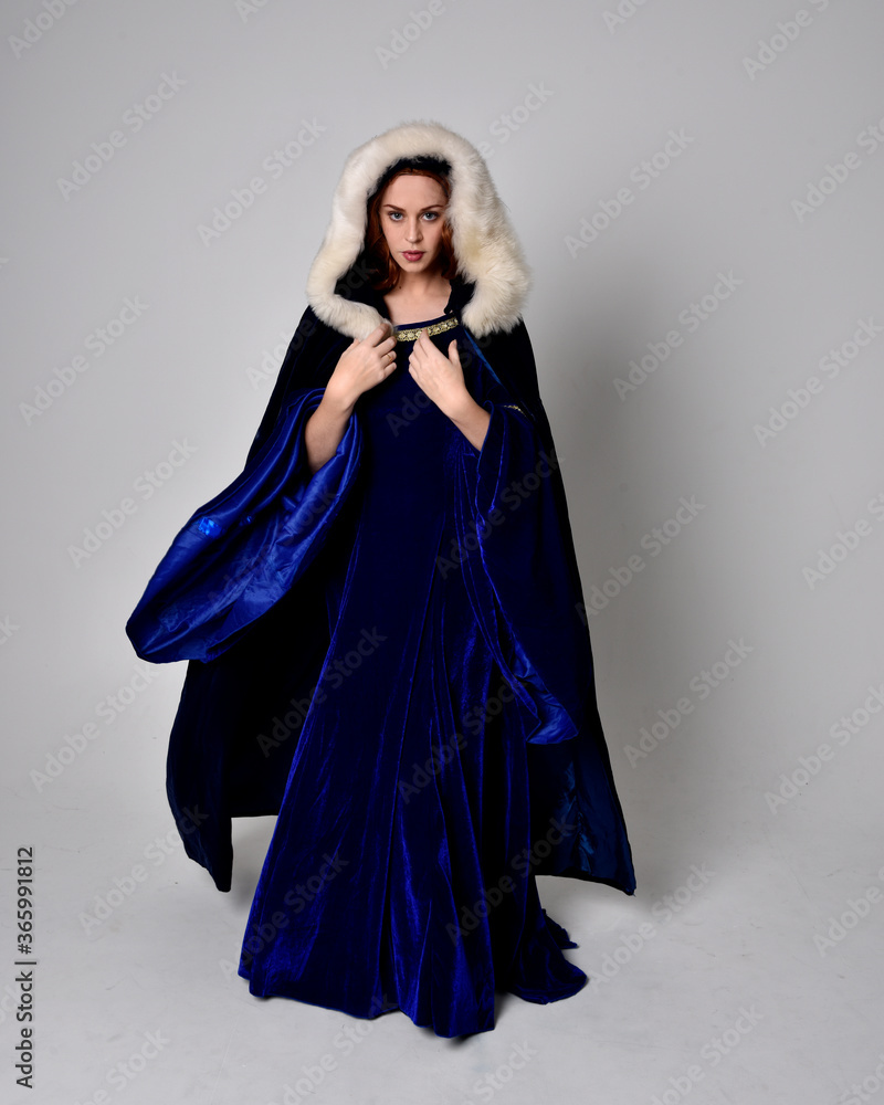 Full length portrait of girl wearing long blue velvet gown with golden crown. sitting pose, isolated against a studio background. Full length portrait of girl wearing long blue velvet gown with golden crown. sitting pose, isolated against a studio background.