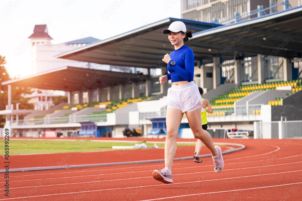 Fototapeta premium Young fitness woman runner jogging excercise in the morning on city stadium track in the city. Female athlete excercise in the city stadium to keep body fitness. Health and recreation stock photo.