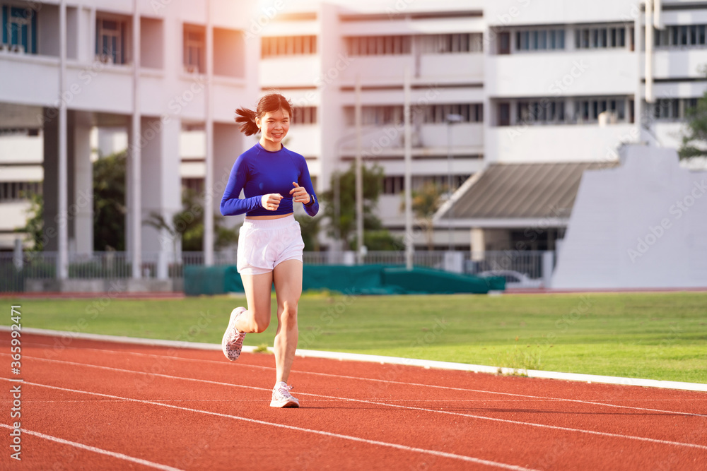 Obraz premium Young fitness woman runner jogging excercise in the morning on stadium track in the city. Female athlete excercise in the city stadium to keep body fitness during COVID-19 pandemic. Stock photo.
