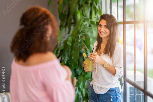 Two Women chatting and smiling while they staying and drinking some beverage