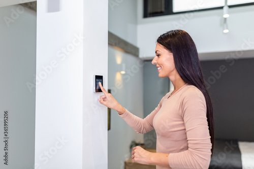 Woman using smart wall home control system in modern apartment. woman touching the display and controlling smart home system hanging on the wall in her apartment