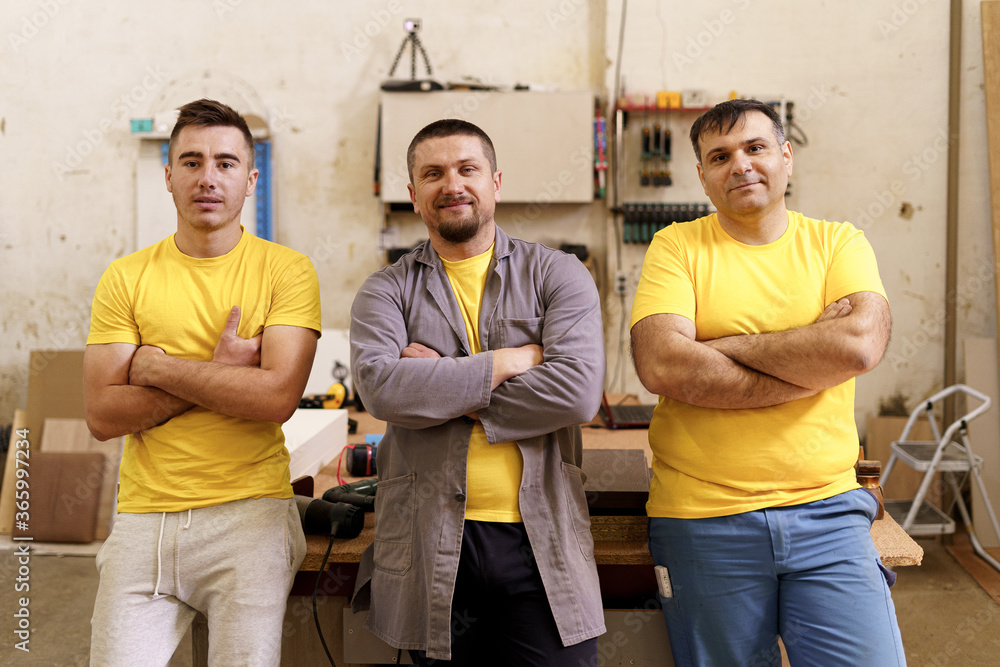 Smiling confident carpenters near their workbench in their workshop looking to camera Smiling confident carpenters near their workbench in their workshop looking to camera