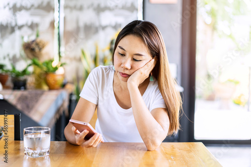 Foto Bored asian woman looking disappointed at her smart phone while waiting someone