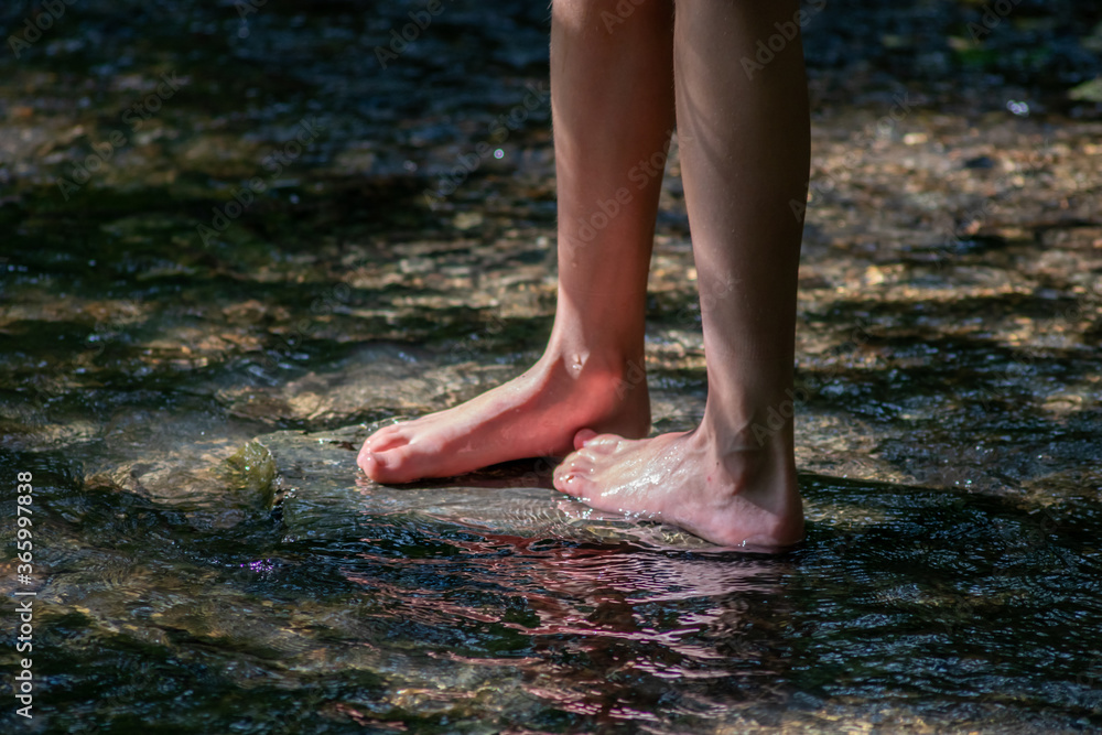 Young boy playing barefoot with clear water at a little creek using his feet and the water spring cooling his toes and legs and refreshing with the pure elixir of life in zen meditation atmosphere