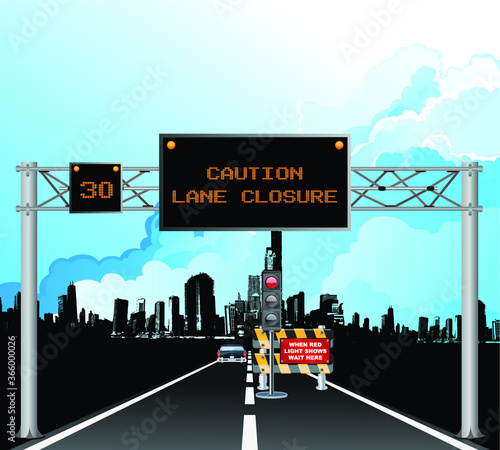 Roadway overhead digital gantry sign with caution roadworks lane closure message and temporary traffic lights set against a blue cloudy sky 