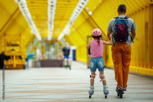 Father and daughter ride roller skates on the yellow bridge