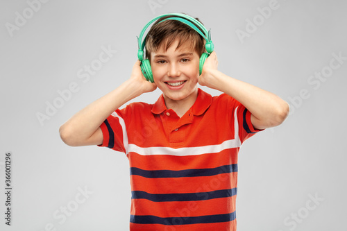 audio equipment and technology people concept - happy smiling boy in headphones listening to music over grey background