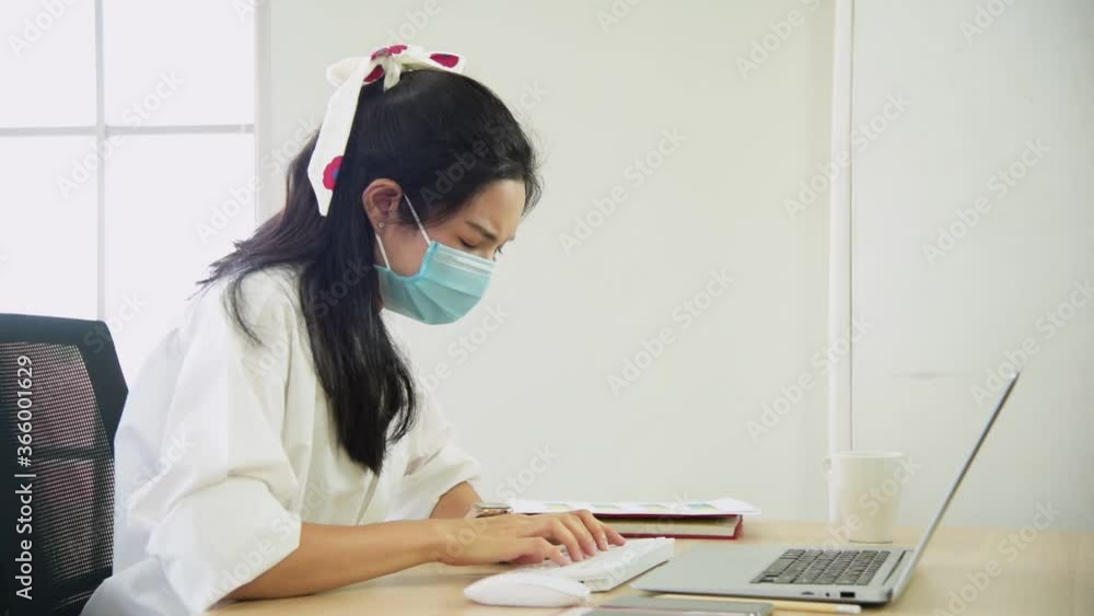 Young Asian woman in casuial outfit wearing mask sitting on work table getting angry and confuse while using computer laptop to working at home Young Asian woman in casuial outfit wearing mask sitting on work table getting angry and confuse while using computer laptop to working at home