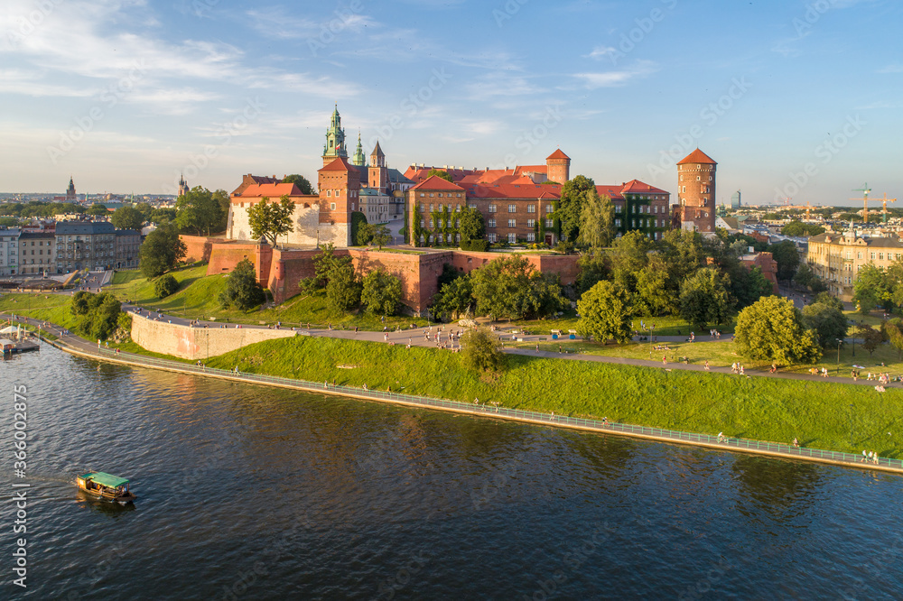 Royal Wawel Cathedral and castle in Krakow, Poland. Aerial view in sunset light. Vistula River, tourist boat, riverbank with park. promenade and  walking people