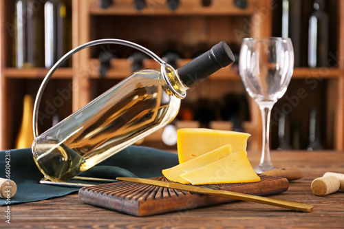 Holder with bottle of wine and cheese on table in cellar
