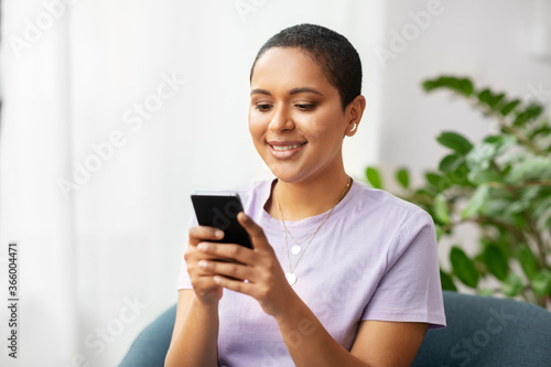 technology and people concept - smiling african american woman in glasses with smartphone at home